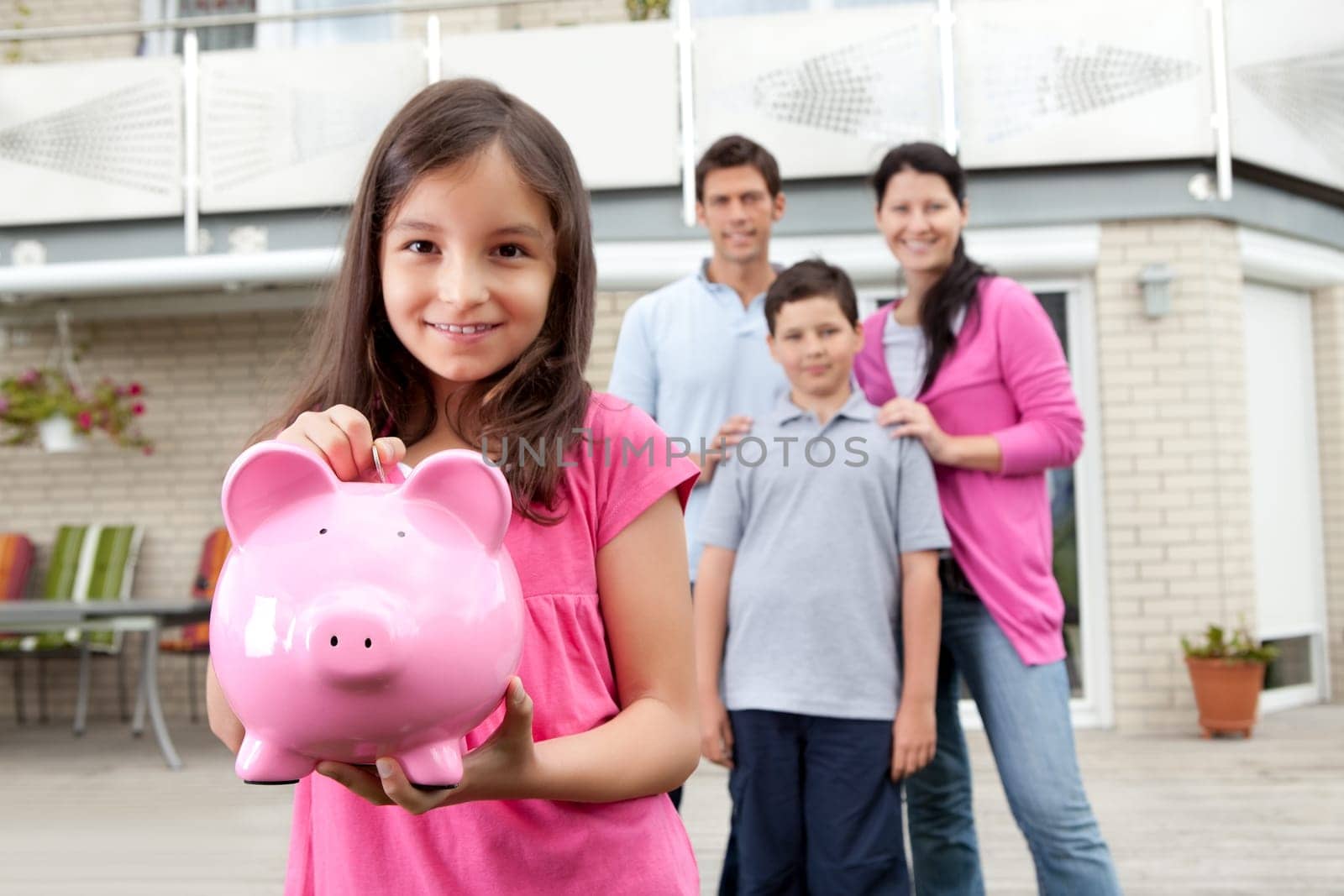 Beautiful little girl inserting coin in a piggy bank with her family in background