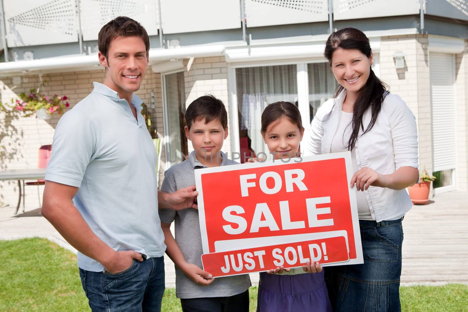 Portrait of happy young family with a sale sign outside their home