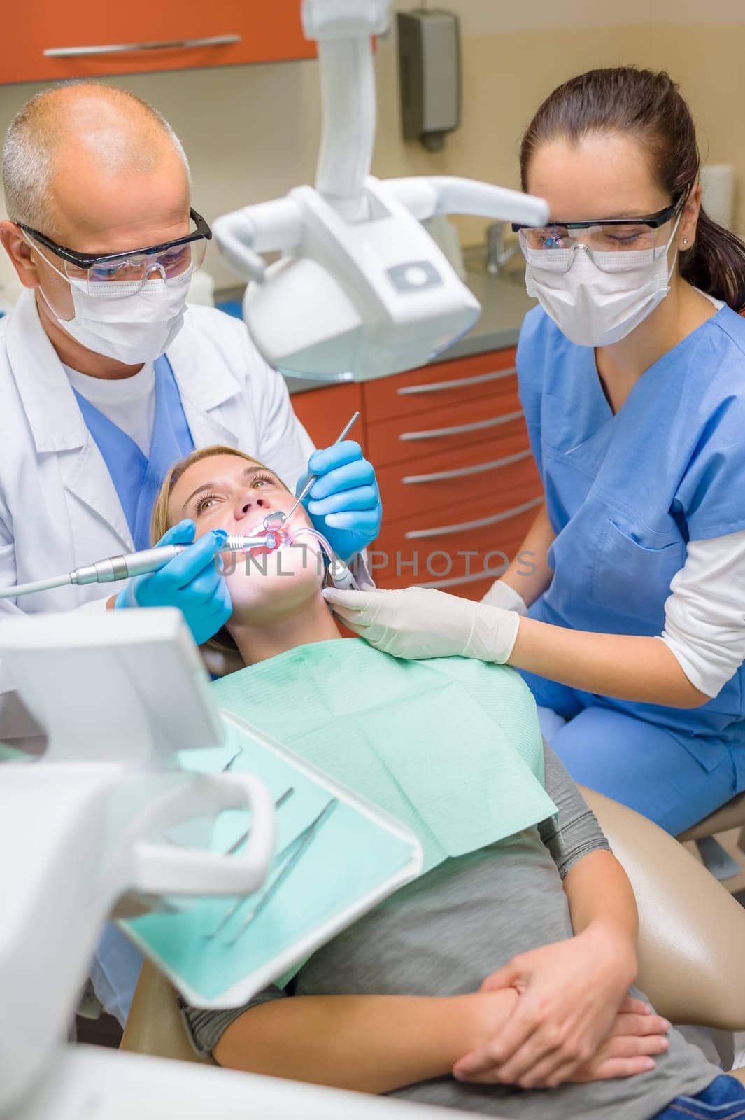 Professional dentist and nurse doing dental treatment on female patient