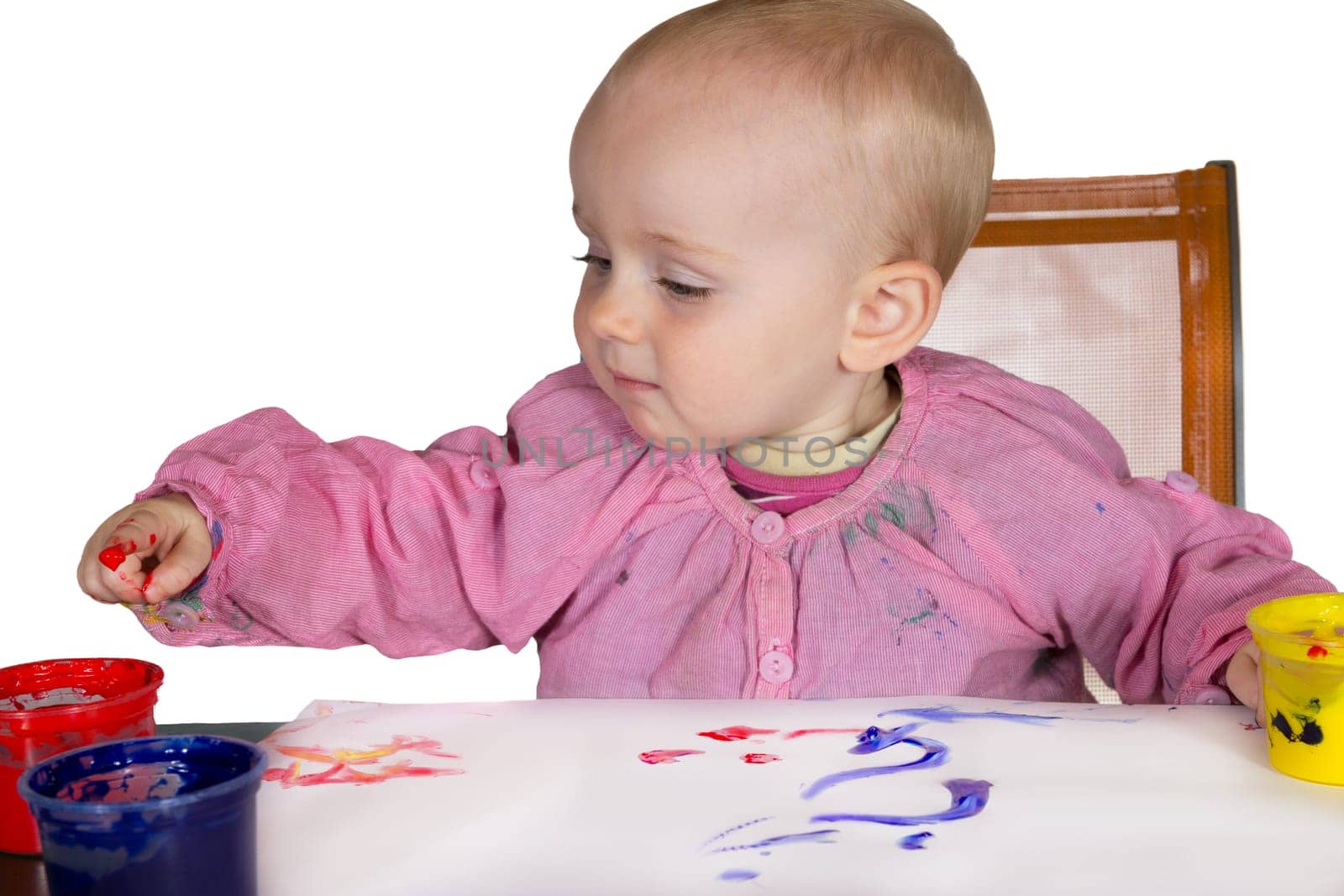 Cute little baby girl experimanting with paint dipping her finger into a jar of pigment to draw on the paper in front of her
