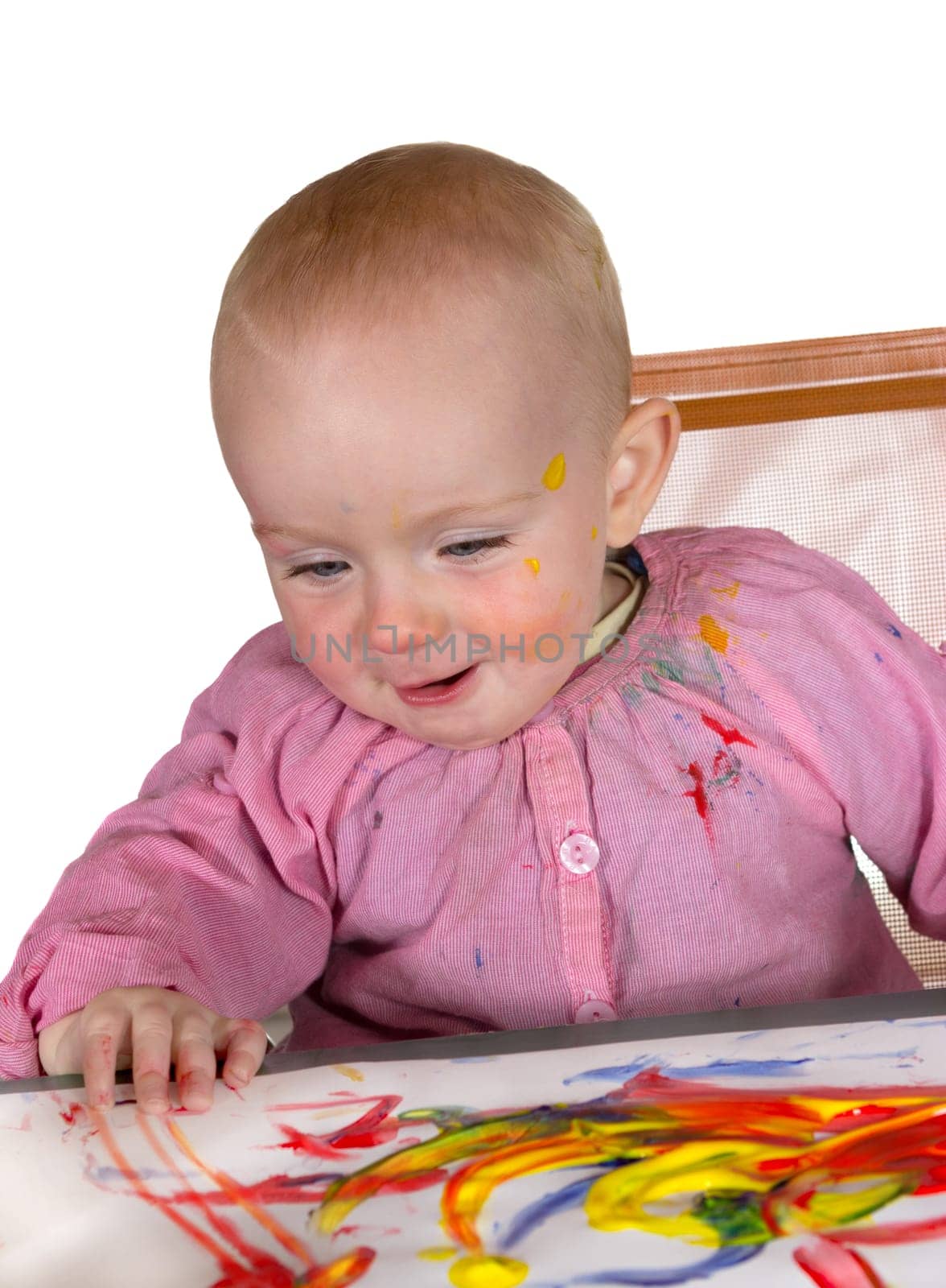 Happy baby girl daubed with colourful red and yellow paint finger painting on a large sheet of paper