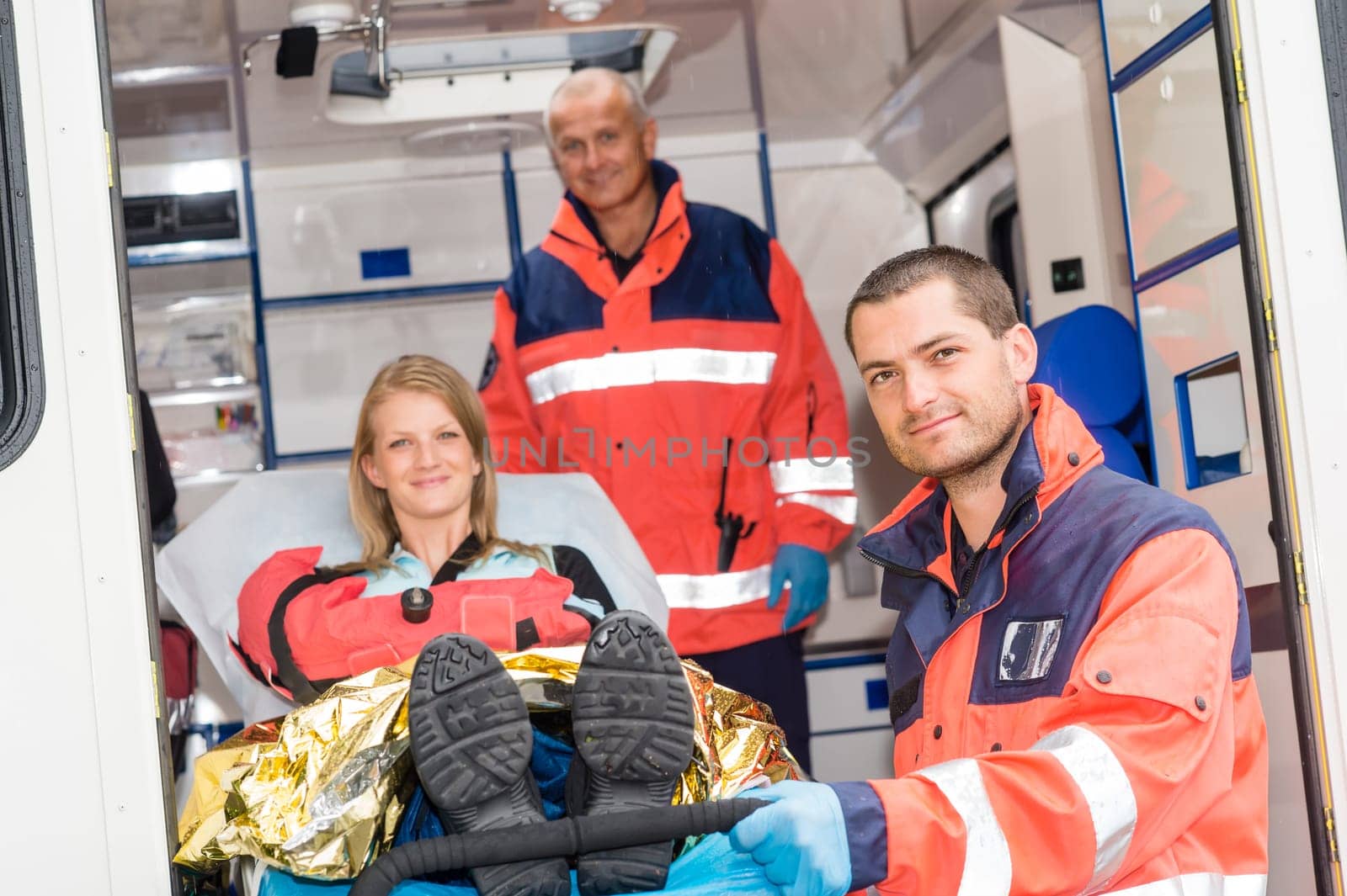 Paramedics helping woman on stretcher in ambulance smiling accident victim