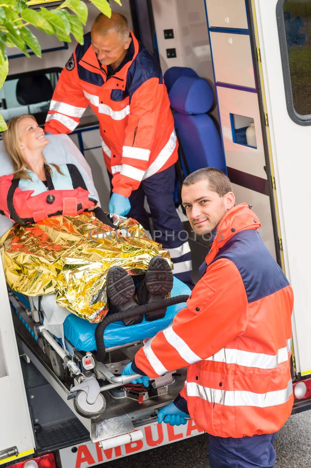 Paramedics helping woman on stretcher in ambulance smiling accident victim