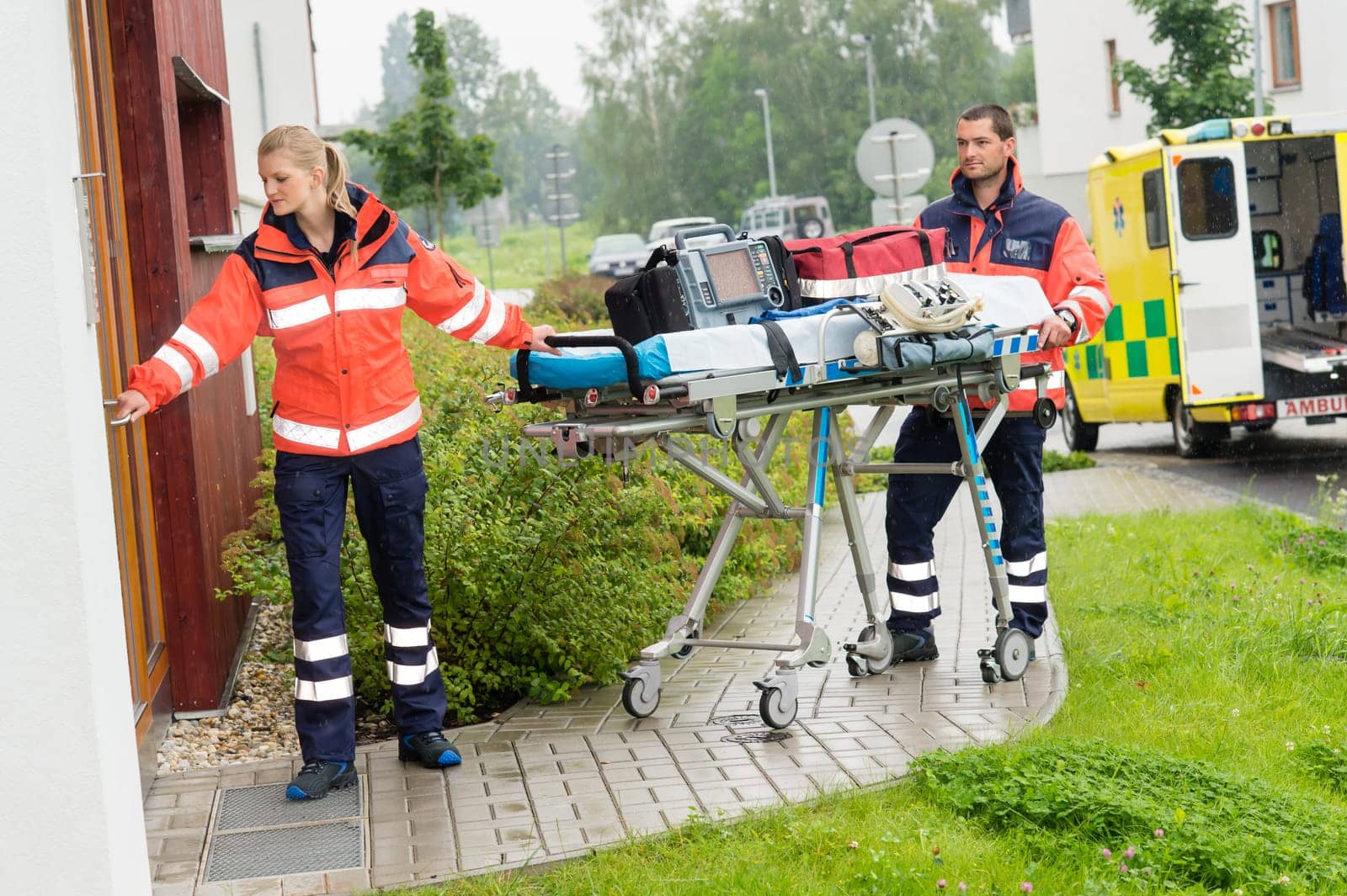 Paramedics carrying emergency stretcher ambulance house call visit door
