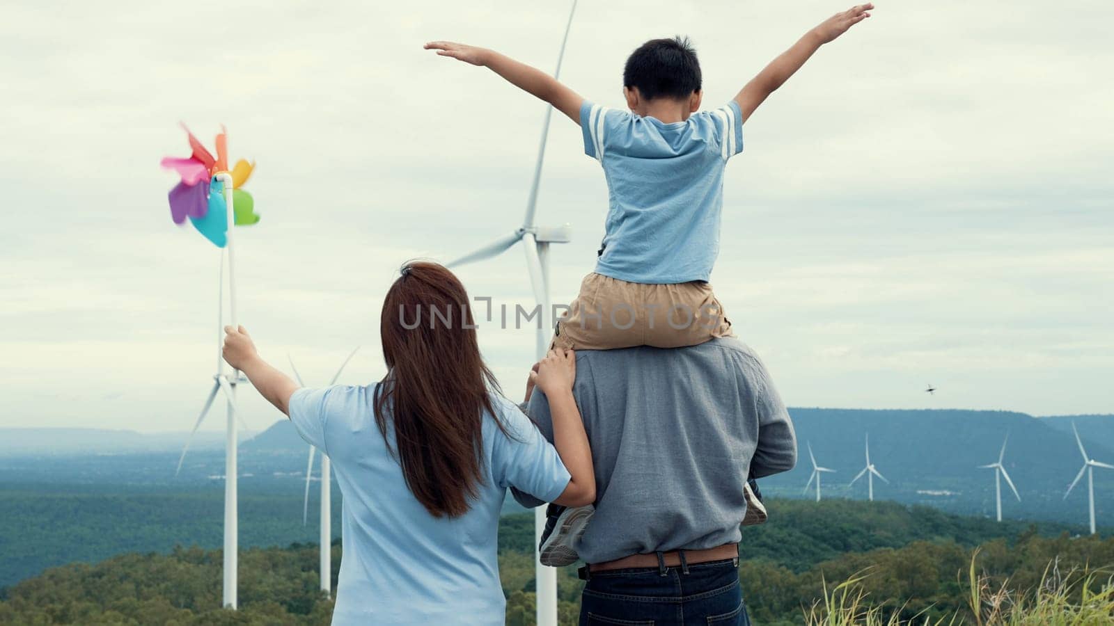 Concept of progressive happy family enjoying their time at the wind turbine farm. Electric generator from wind by wind turbine generator on the country side with hill and mountain on the horizon.