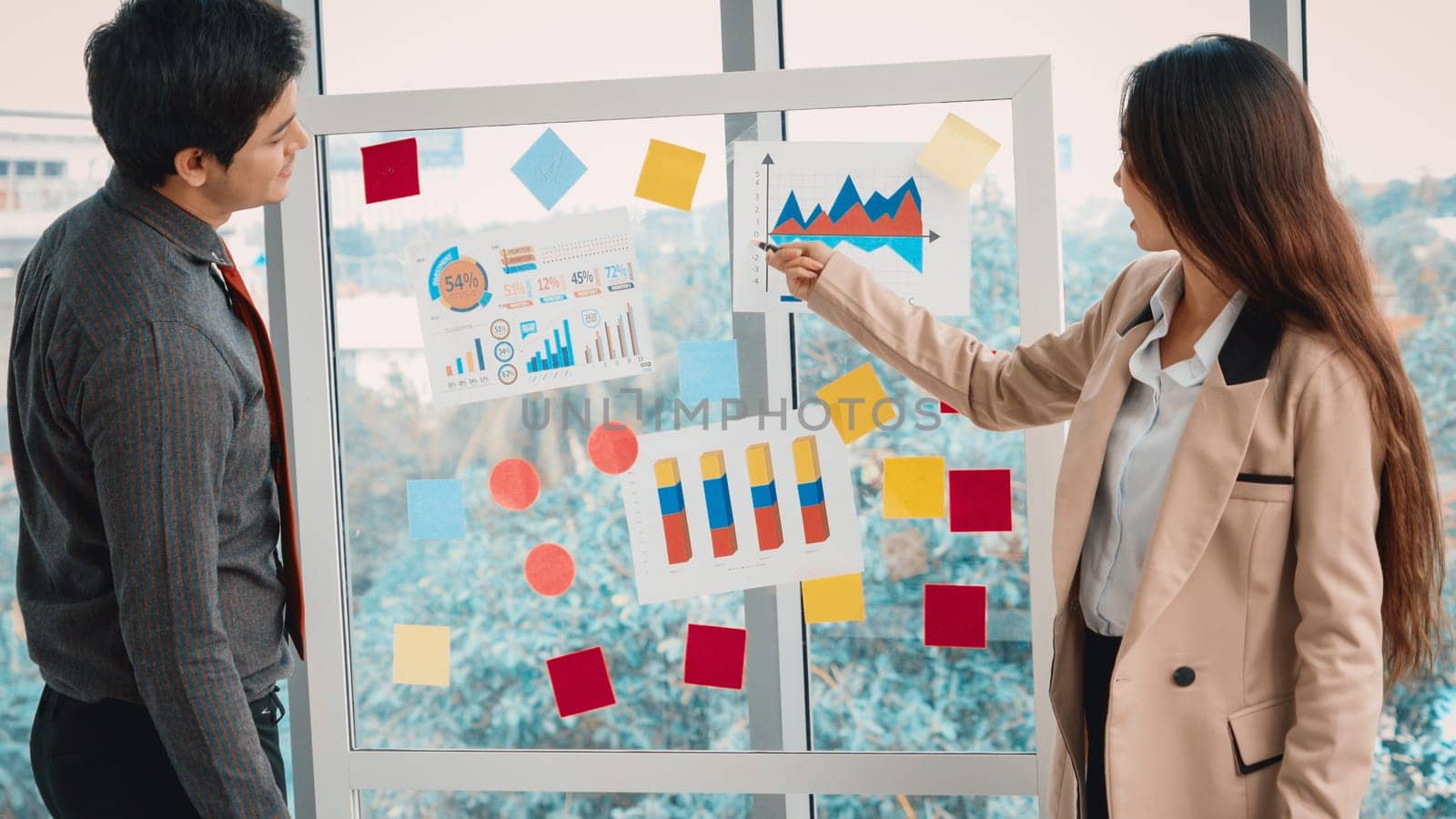 Business people work on project planning board in office and having conversation with coworker friend to analyze project development . They use sticky notes posted on glass to make it organized. Jivy