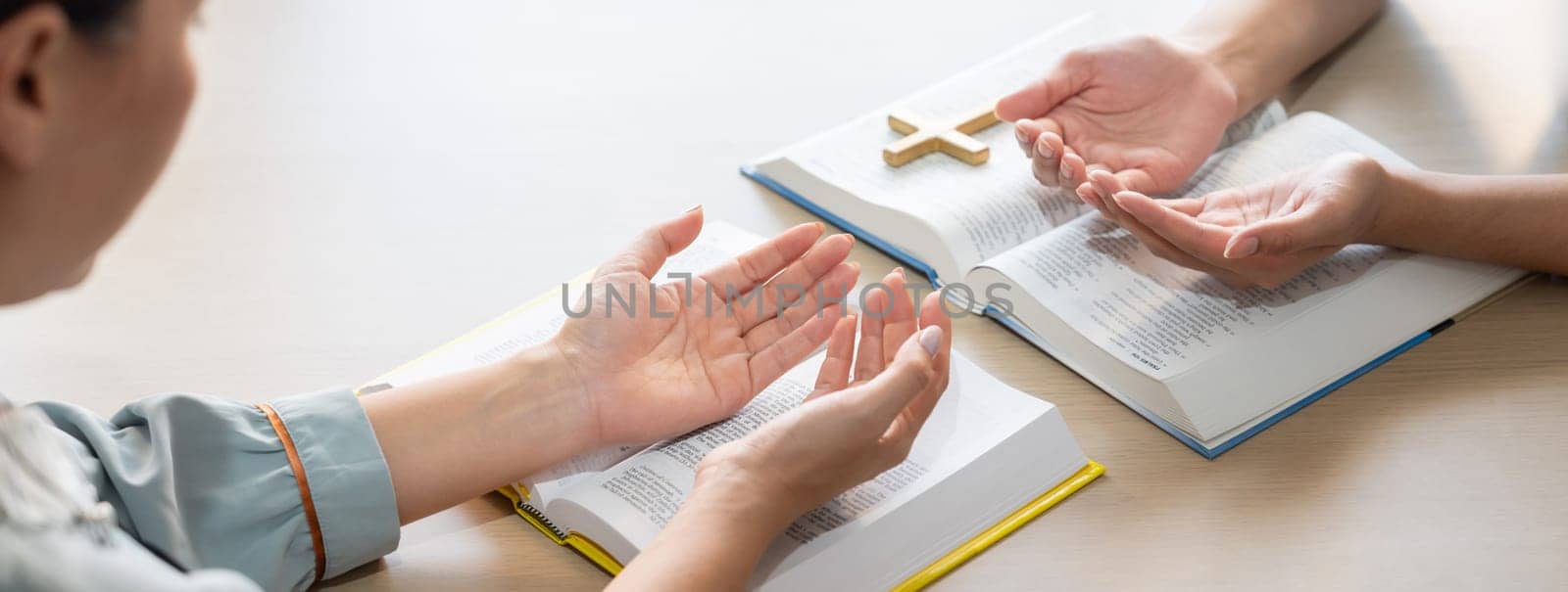 Two believer praying together on holy bible book faithfully with wooden cross placed at wooden church. Concept of hope, religion, faith, christianity and god blessing. Facing hand. Burgeoning.