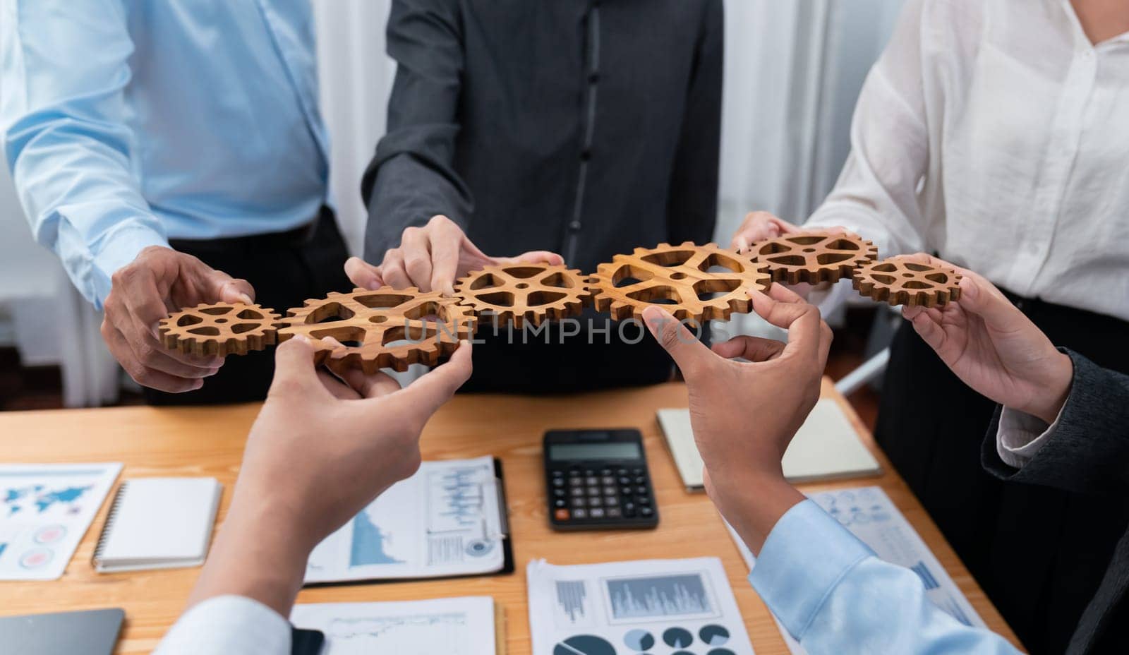 Office worker holding cog wheel as unity and system teamwork in corporate workplace with piles of business paper and financial report on meeting table. Business people with business success. Concord