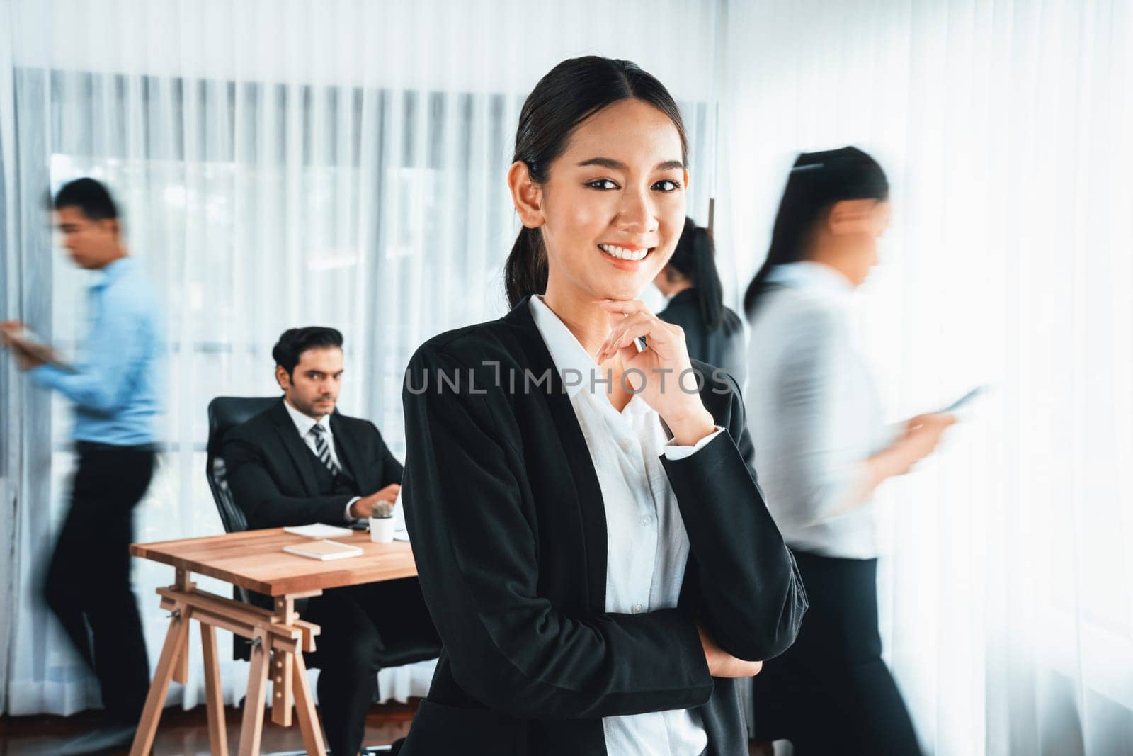 Portrait of happy young asian businesswoman looking at camera with motion blur background of business people movement in dynamic business meeting. Habiliment
