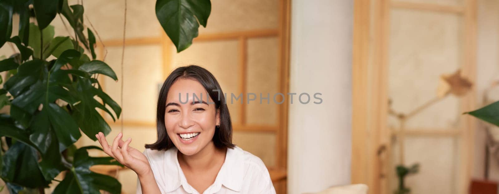 Stylish young woman in cafe with coffee, holding mobile phone, laughing and smiling. Lifestyle and people concept.