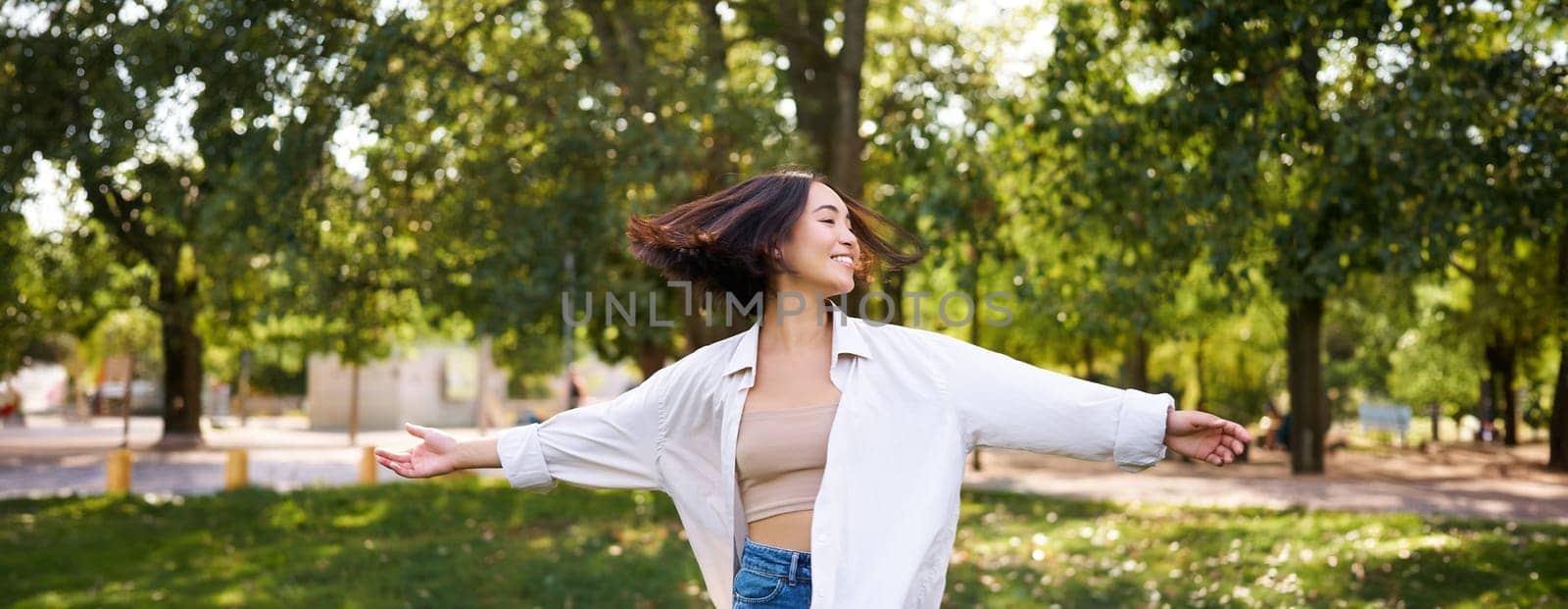 Freedom and people concept. Happy young asian woman dancing in park around trees, smiling and enjoying herself.