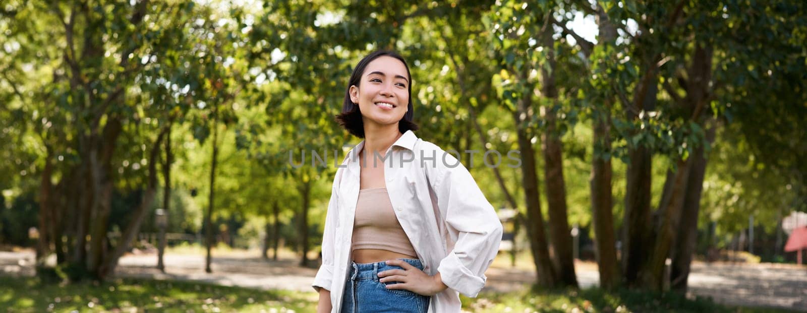 Modern people. Happy young asian girl walking in park, smiling and enjoying beautiful summer day.