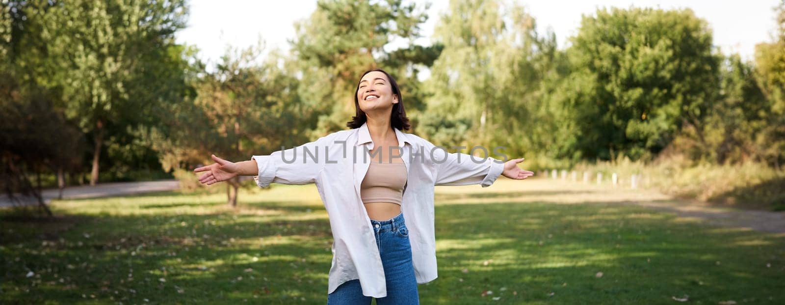Carefree asian girl laughing and dancing in park, enjoying summer sunny day, raising hands up and breathing fresh air by Benzoix