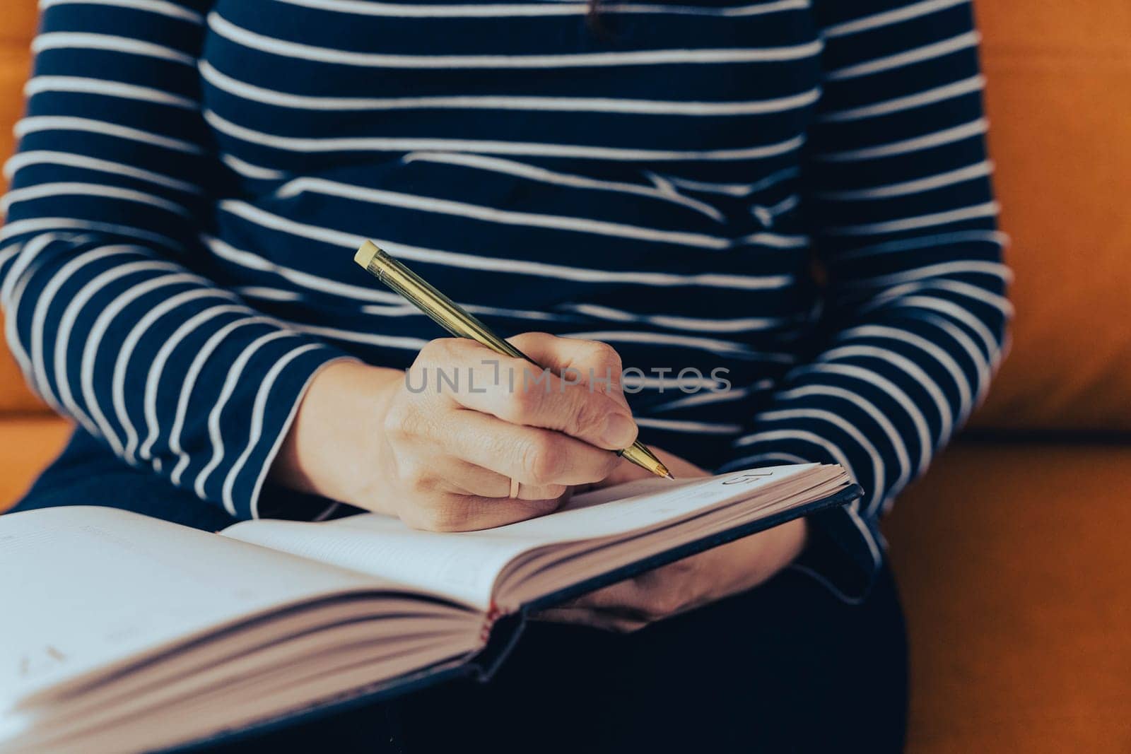 a woman makes notes of her thoughts in a notebook. She is sitting on the sofa in her home in a cozy atmosphere, which contributes to creating an ideal atmosphere for immersion in her thoughts and reports.