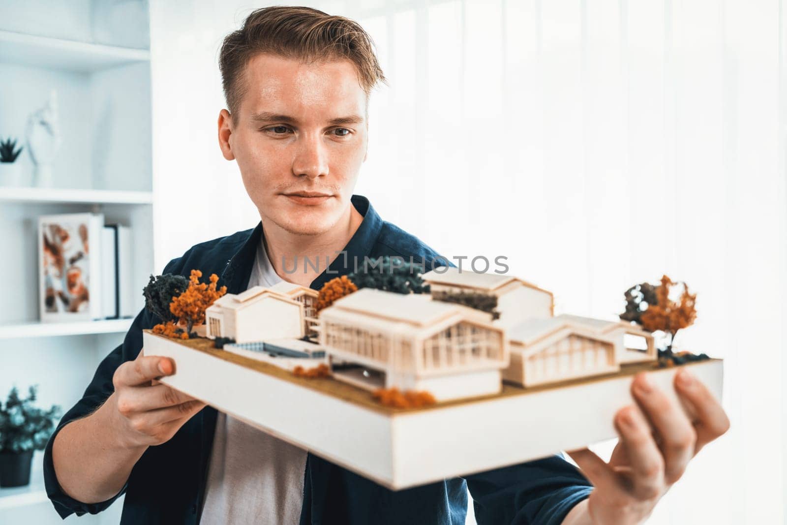 Architect designer studies elegant while holding house model, reviewing structure design for improvement with construction plan on table. Creativity and innovation in architectural design. Iteration