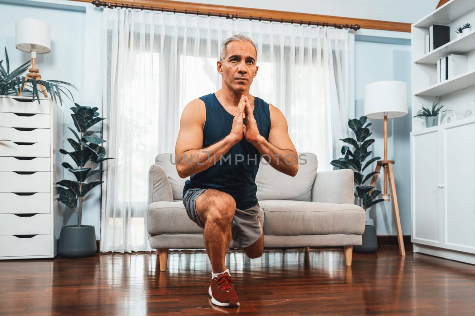 Active and fit senior man warmup and stretching using furniture before home exercising routine at living room. Healthy fitness lifestyle concept after retirement for pensioner. Clout