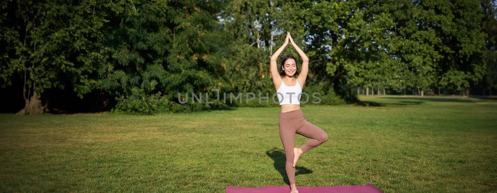 Portrait of young asian woman stretching, doing yoga on rubber mat, exercising in park, mindful training on fresh air.