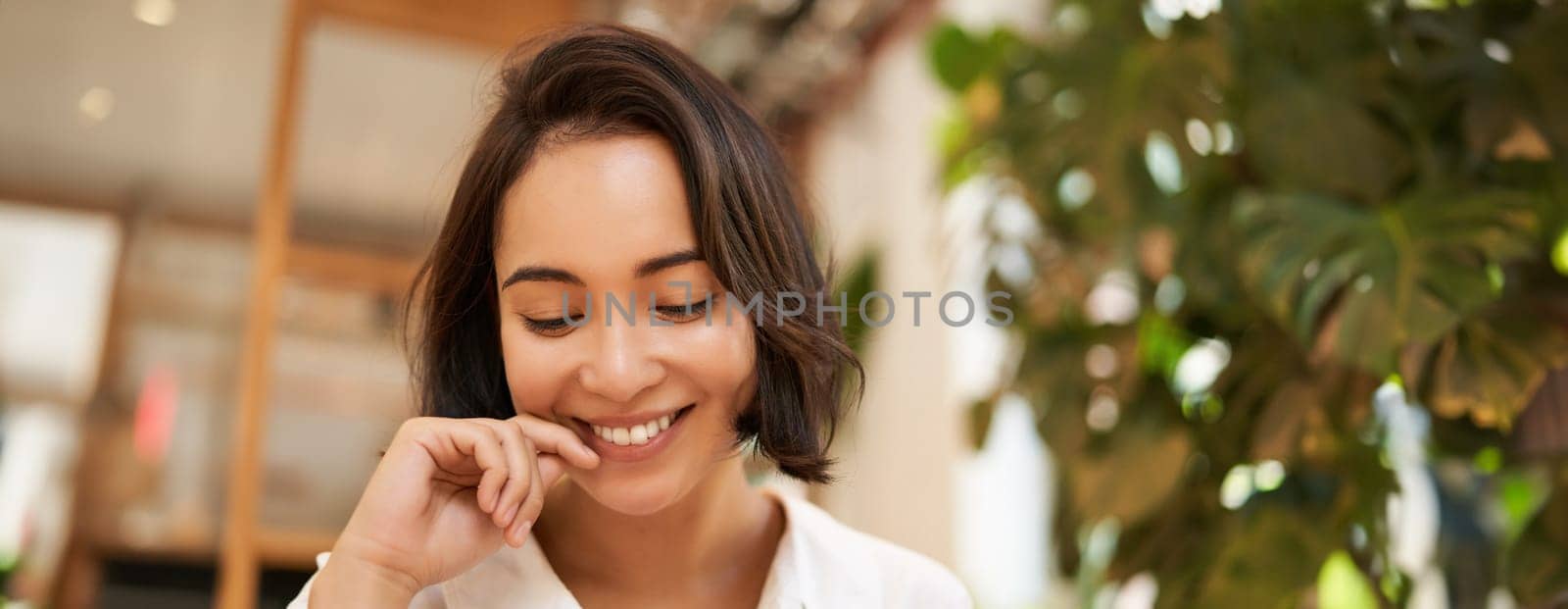 Close up portrait of beautiful, romantic young asian woman, smiling and looking happy, sitting in cozy cafe by Benzoix