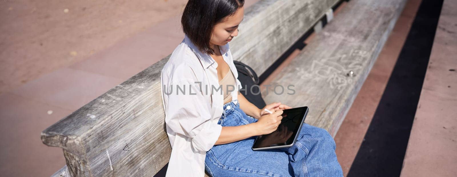 Portrait of young artist, asian girl drawing in digital tablet with graphic pen, sitting outdoors in park, getting inspiration by Benzoix