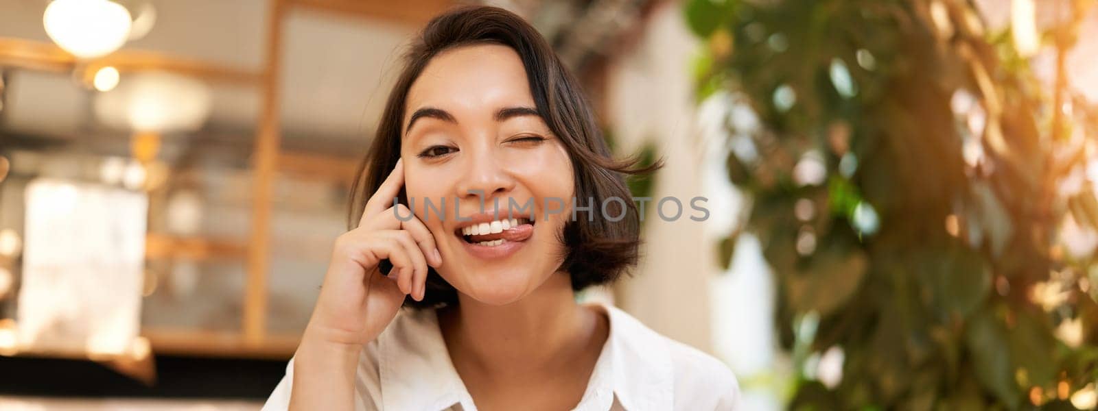 Close up portrait of funny young asian woman, sitting in cafe, chatting lively, smiling at camera.