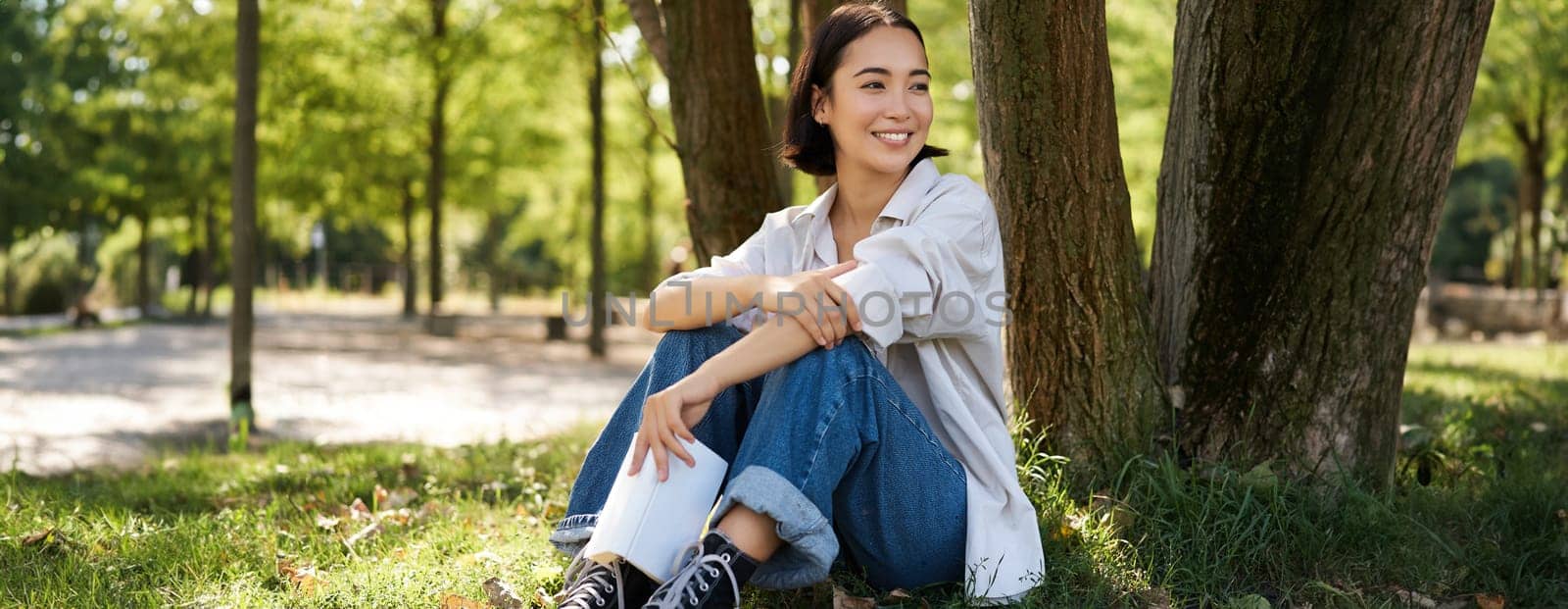 Woman sitting in park with her favourite book, leaning on tree under shade on sunny day, enjoying nature and calm relaxing atmosphere by Benzoix