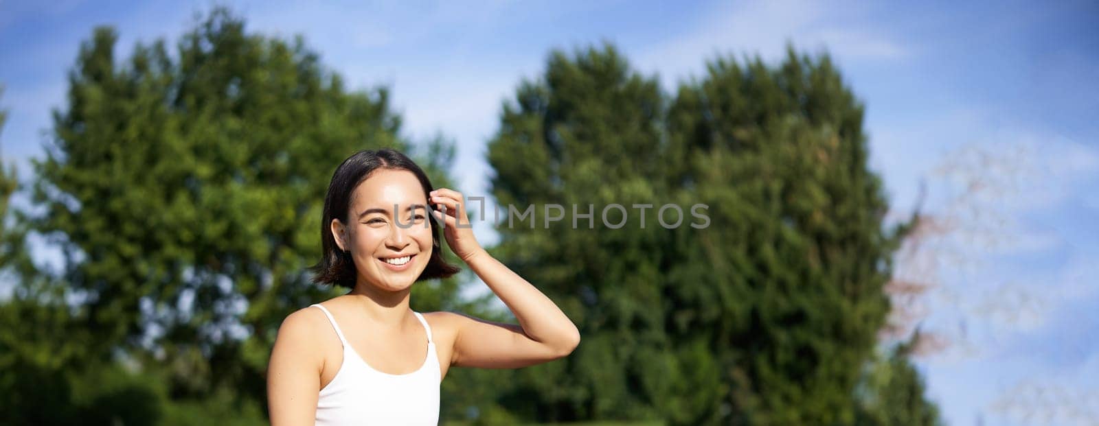 Meditation and mindfulness. Young asian woman smiling on fitness mat in park, doing yoga training, meditating on fresh air.