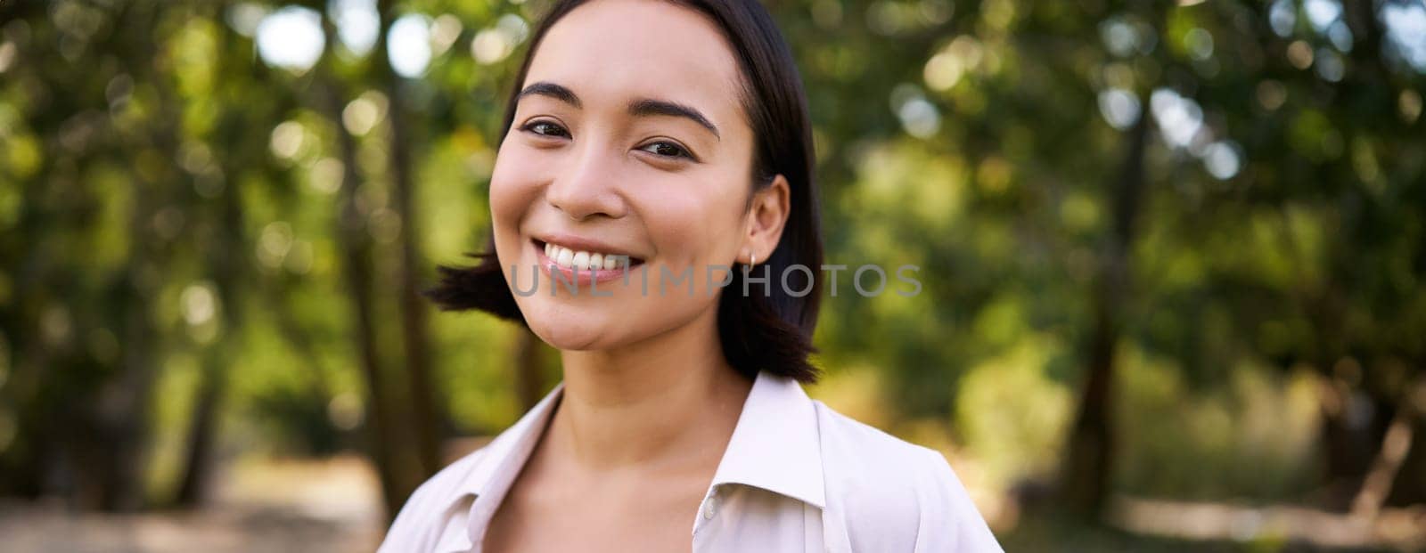 People concept. Smiling asian girl looking at camera with happy, joyful emotion, posing in green park on a warm summer day.