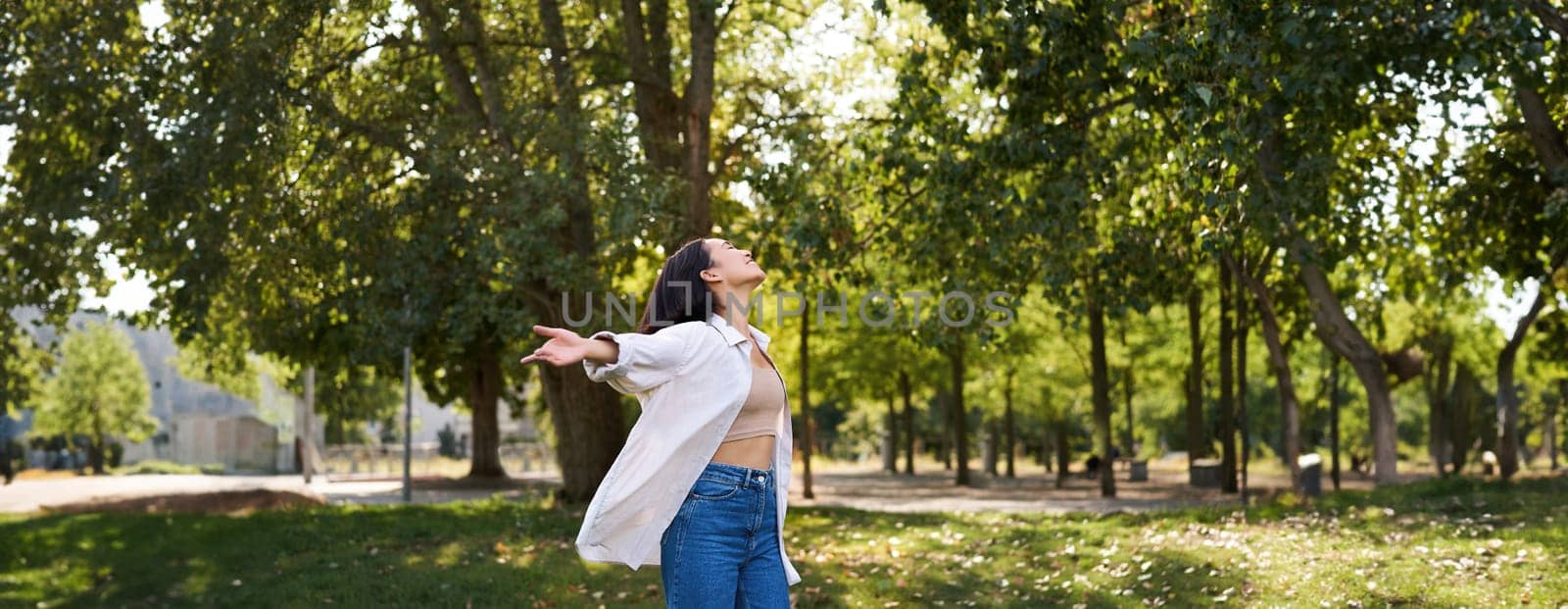 Carefree asian girl dancing, feeling happiness and joy, enjoying the sun on summer day, walking in park with green trees by Benzoix