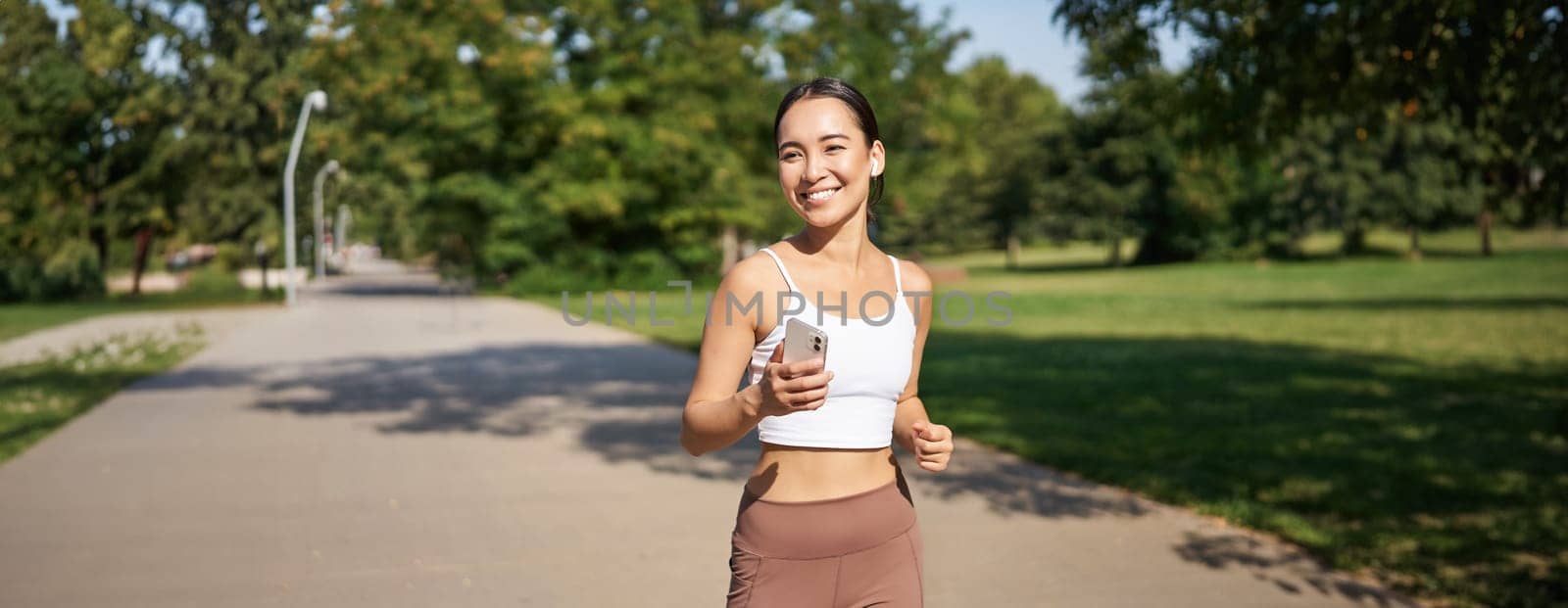 Happy smiling asian woman jogging in park. Healthy young female runner doing workout outdoors, running on streets by Benzoix