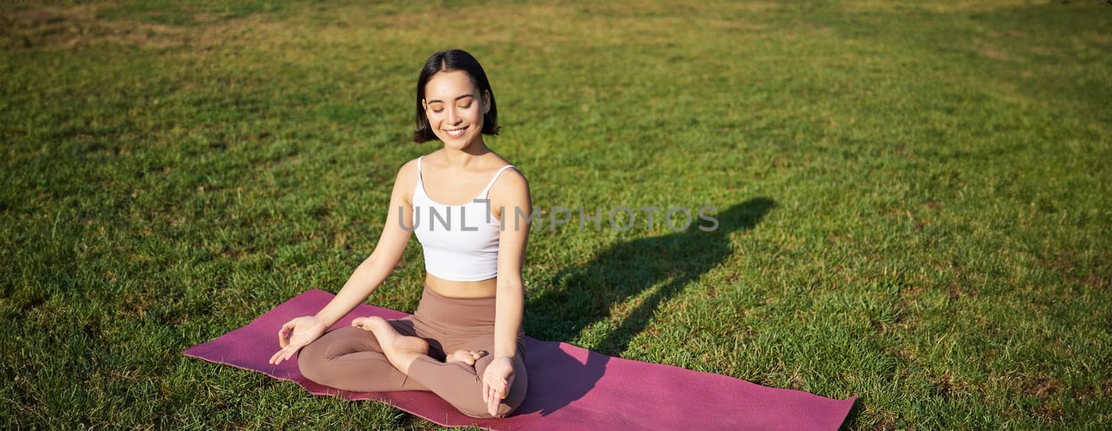 Portrait of young mindful woman, practice yoga, exercising, inhale and exhale on fresh air in park, sitting on rubber mat by Benzoix