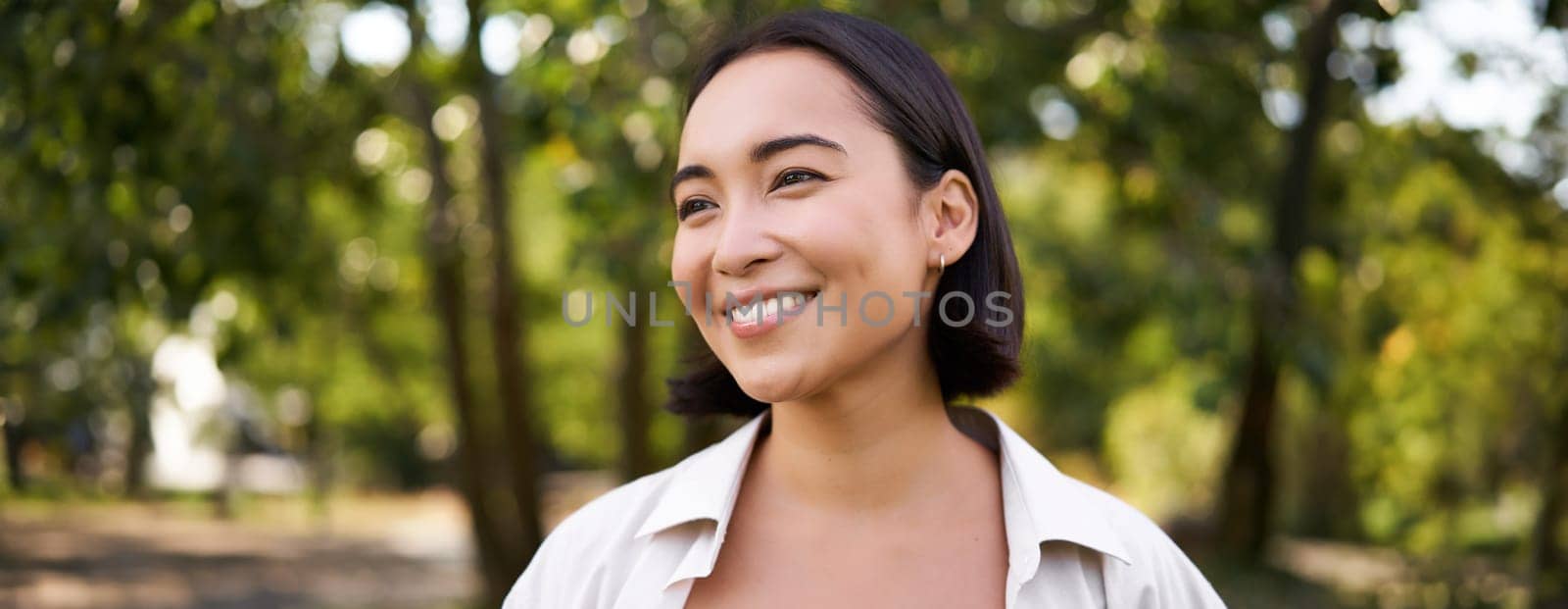 People concept. Smiling asian girl looking at camera with happy, joyful emotion, posing in green park on a warm summer day.