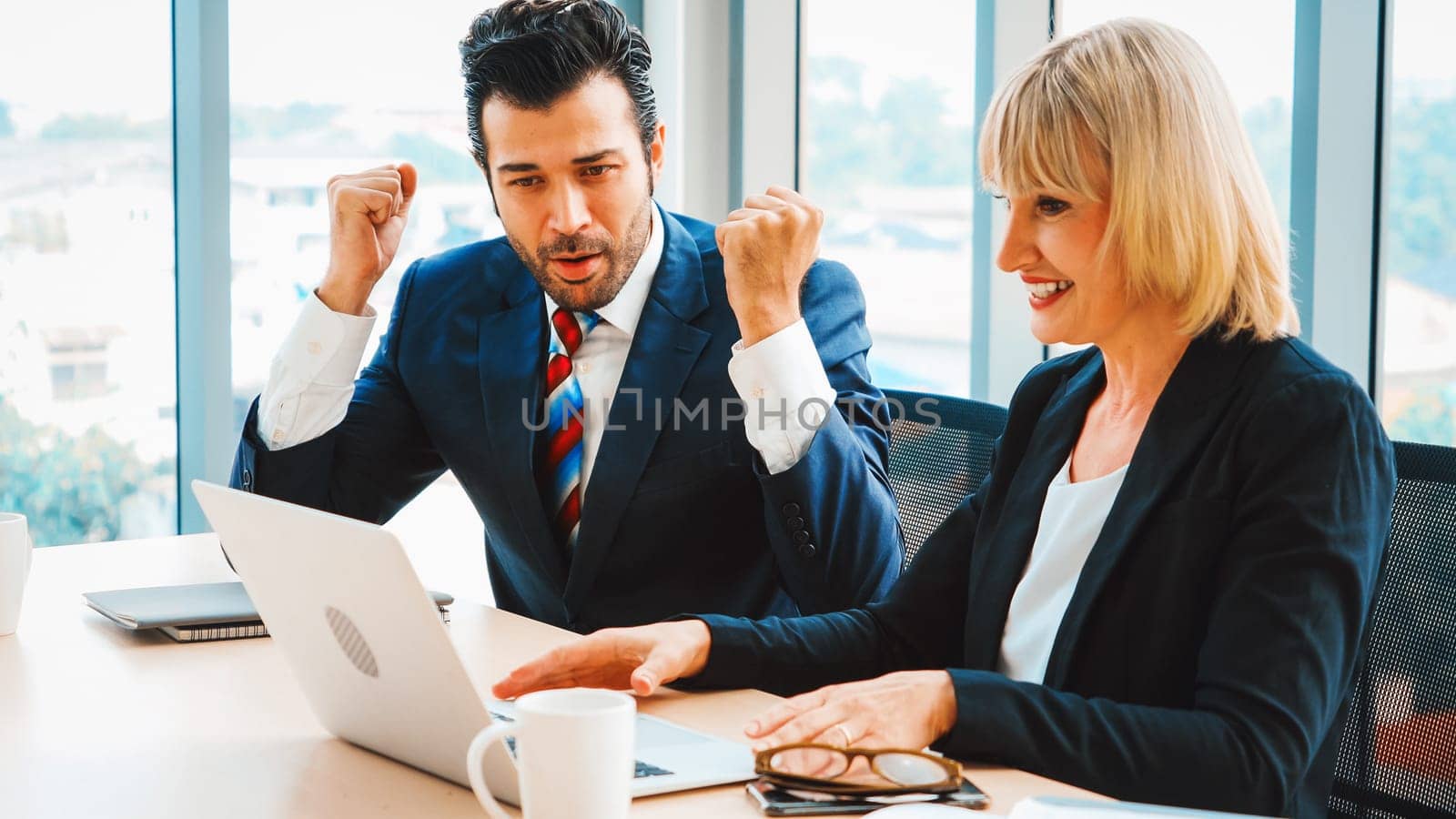 Two happy business people celebrate at office meeting room. Successful businessman congratulate project success with colleague at modern workplace while having conversation on financial report. Jivy