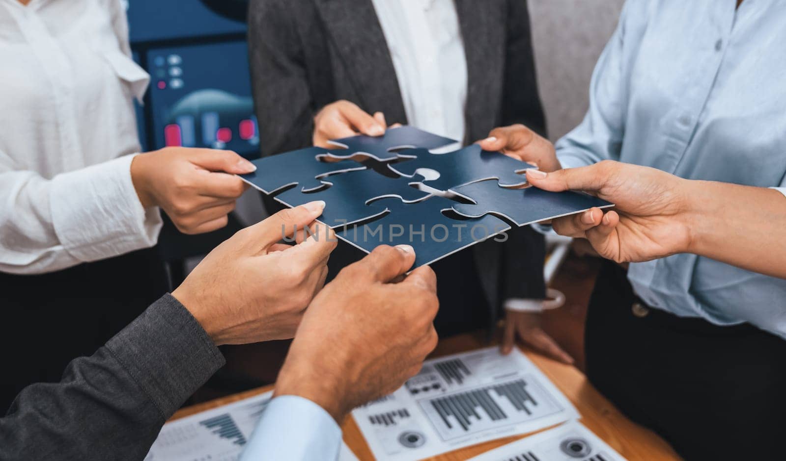 Corporate officer worker collaborate in office, connecting puzzle pieces with report paper on table as partnership and teamwork. Unity and synergy in business concept by merging jigsaw puzzle. Concord