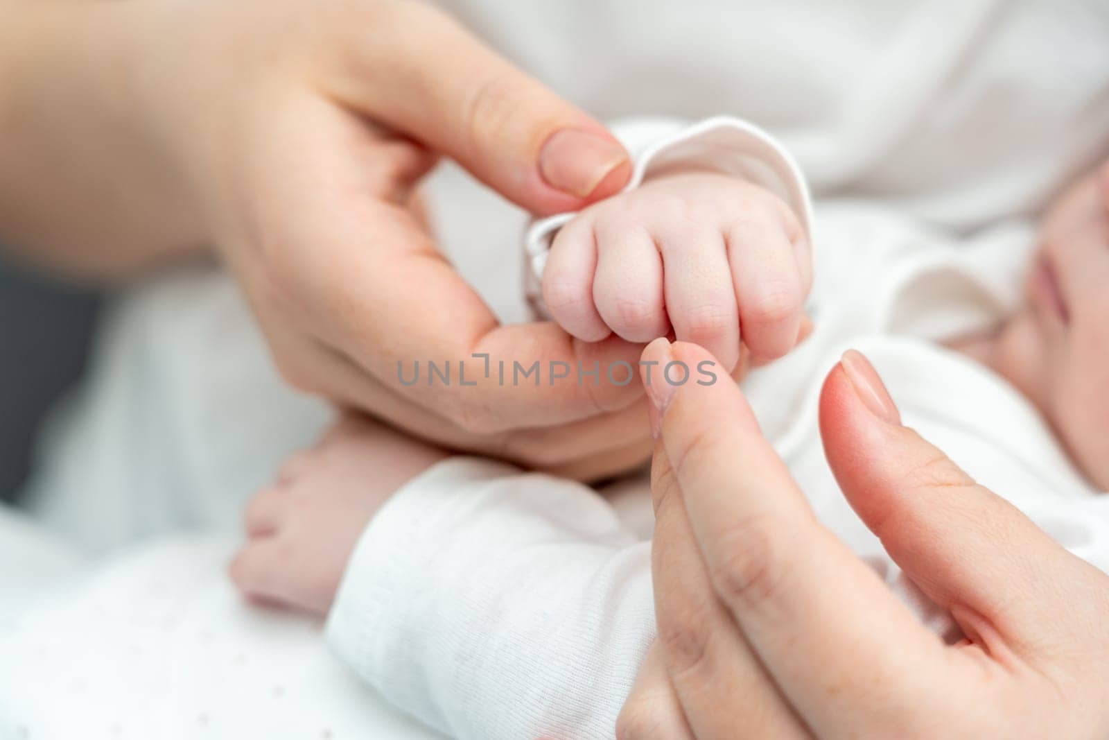 Tiny newborn hand tenderly holds onto mother's finger, portraying the depth of the unbreakable mother-infant bond