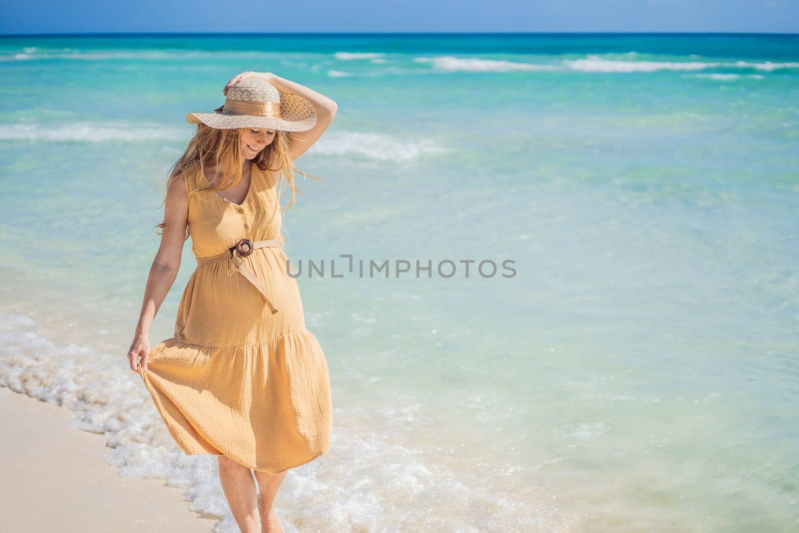 Radiant and expecting, a pregnant woman stands on a pristine snow-white tropical beach, celebrating the miracle of life against a backdrop of natural beauty.