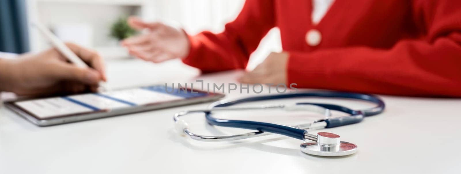 Focused stethoscope on office desk with blurred background of patient attending to doctor appointment at clinic or hospital discussing medical treatment or examining symptoms. Panorama Rigid