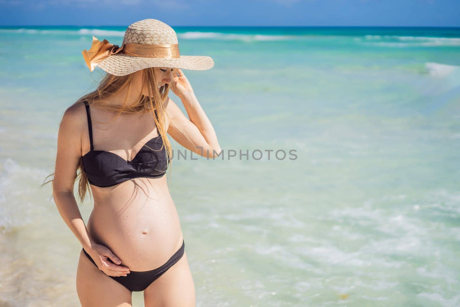 Radiant and expecting, a pregnant woman stands on a pristine snow-white tropical beach, celebrating the miracle of life against a backdrop of natural beauty.