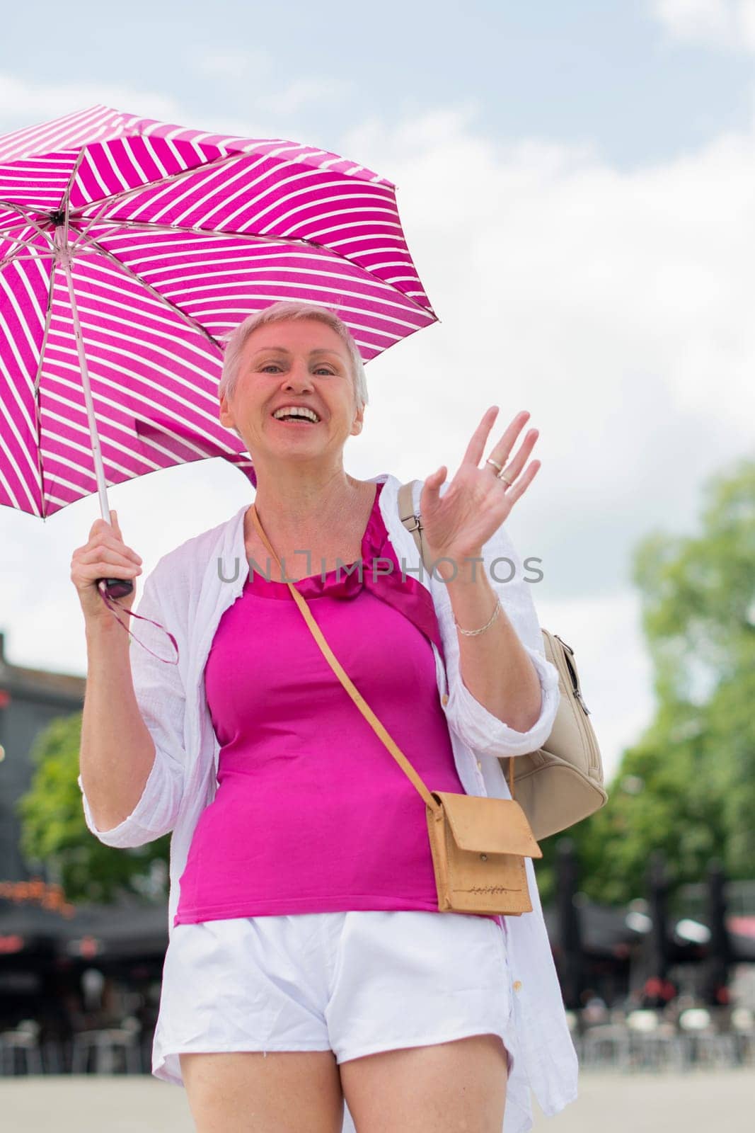 middle-aged woman with a short haircut with an umbrella protecting from the scorching sun looks at the camera and laughs, High Quality Photo
