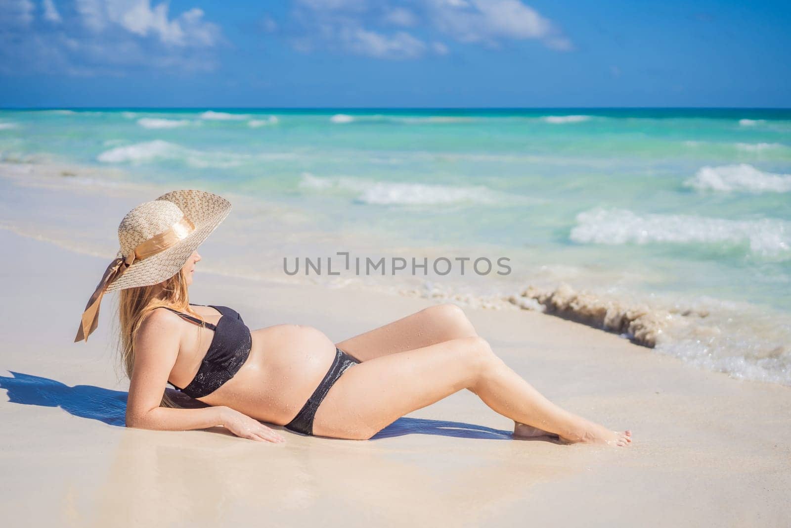 Radiant and expecting, a pregnant woman stands on a pristine snow-white tropical beach, celebrating the miracle of life against a backdrop of natural beauty by galitskaya