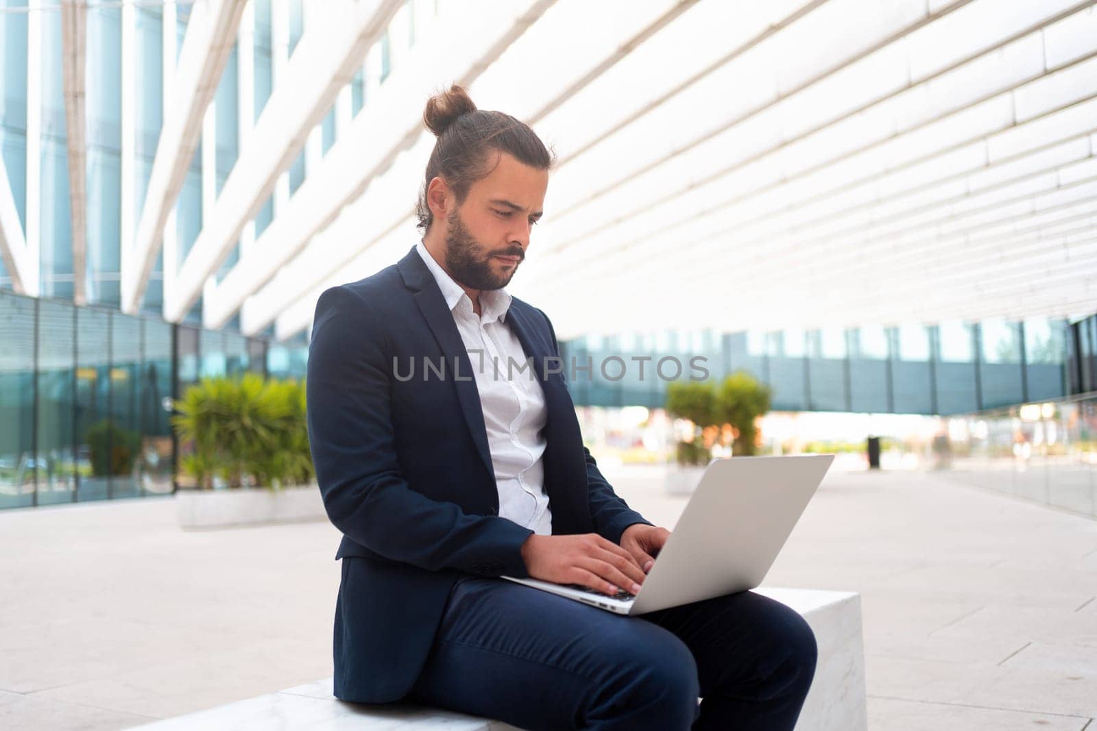 Business on the Go Businessman Working on his Laptop on the Street near office building. Handsome hispanic business person sitting use laptop. Confident male manager working outdoor.