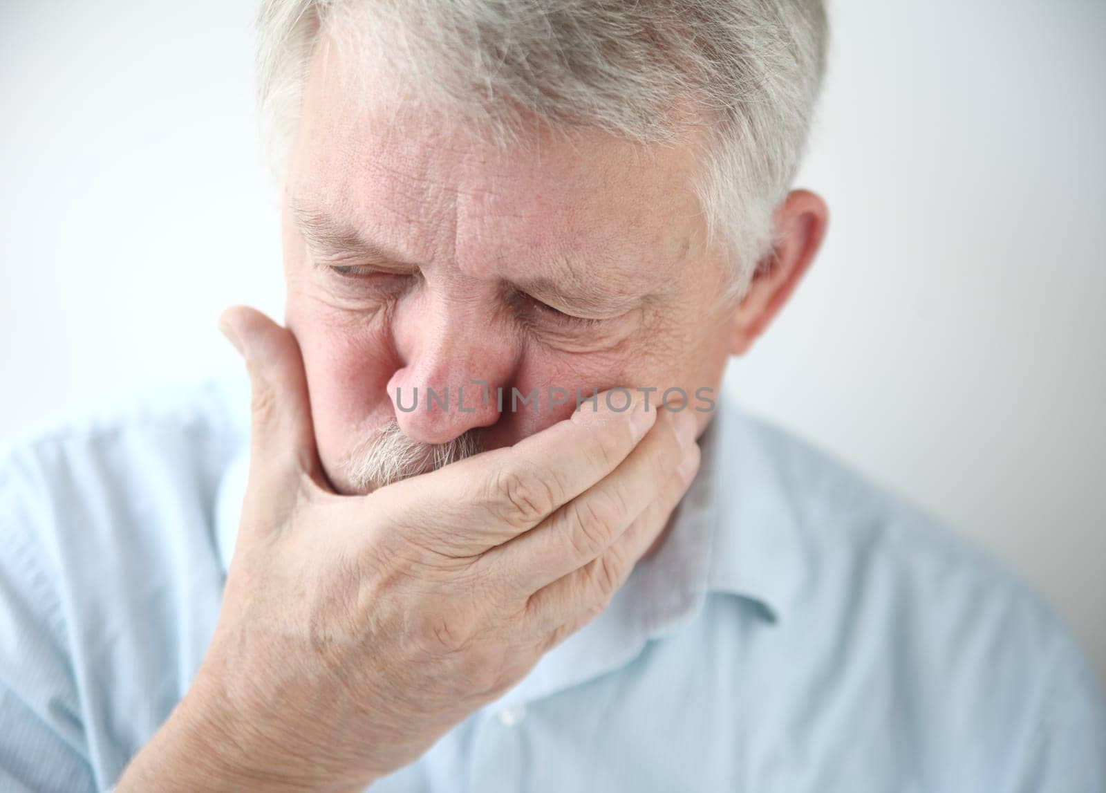 senior man holds his hand to his mouth while feeling nauseous