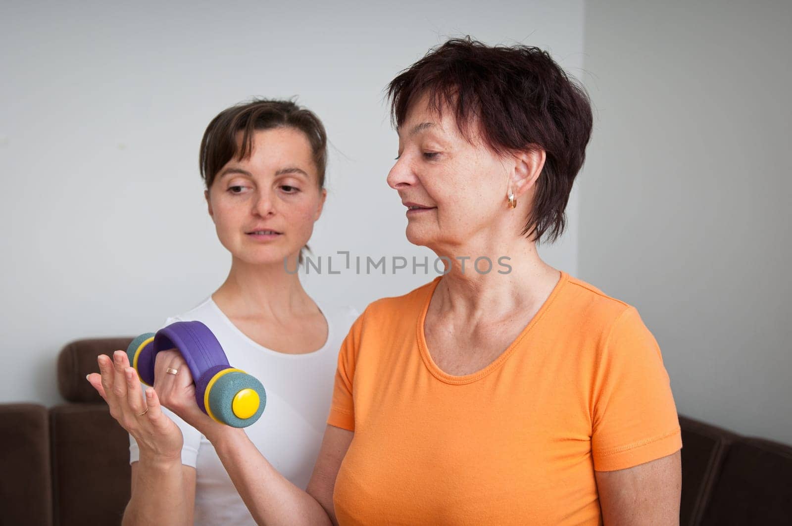 Smiling senior fitness woman exercising with barbells assisted by coach