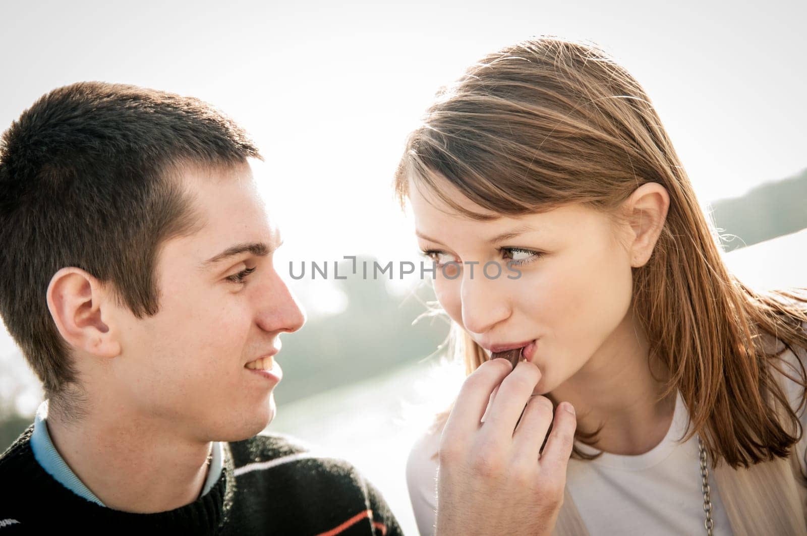Young happy couple together outdoor - man gives chcolate to woman