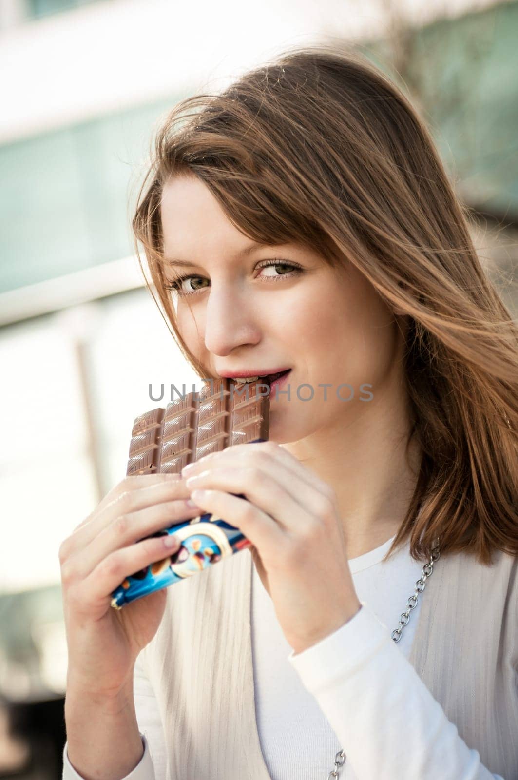 Lifestyle outdoor scene - young beautiful woman eating chocolate