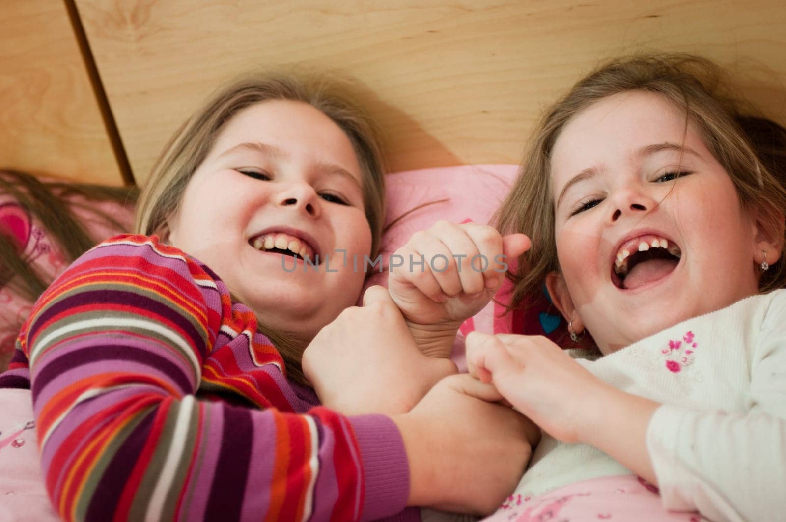 Cute children (two sisters) laughing at home lying in bed