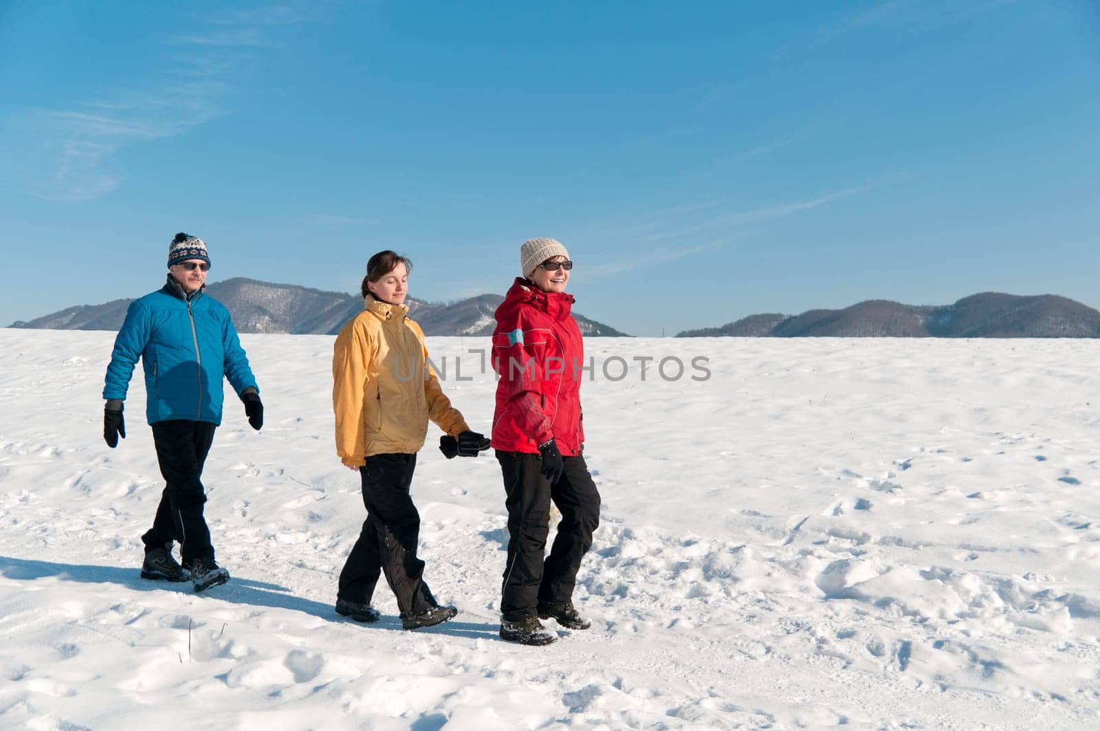 Family together - senior couple walking with ther adult child in winter nature