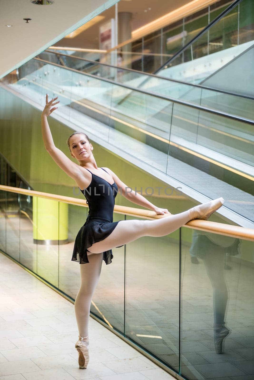 Ballet dancer (ballerina) dancing in modern shopping premises at escalator
