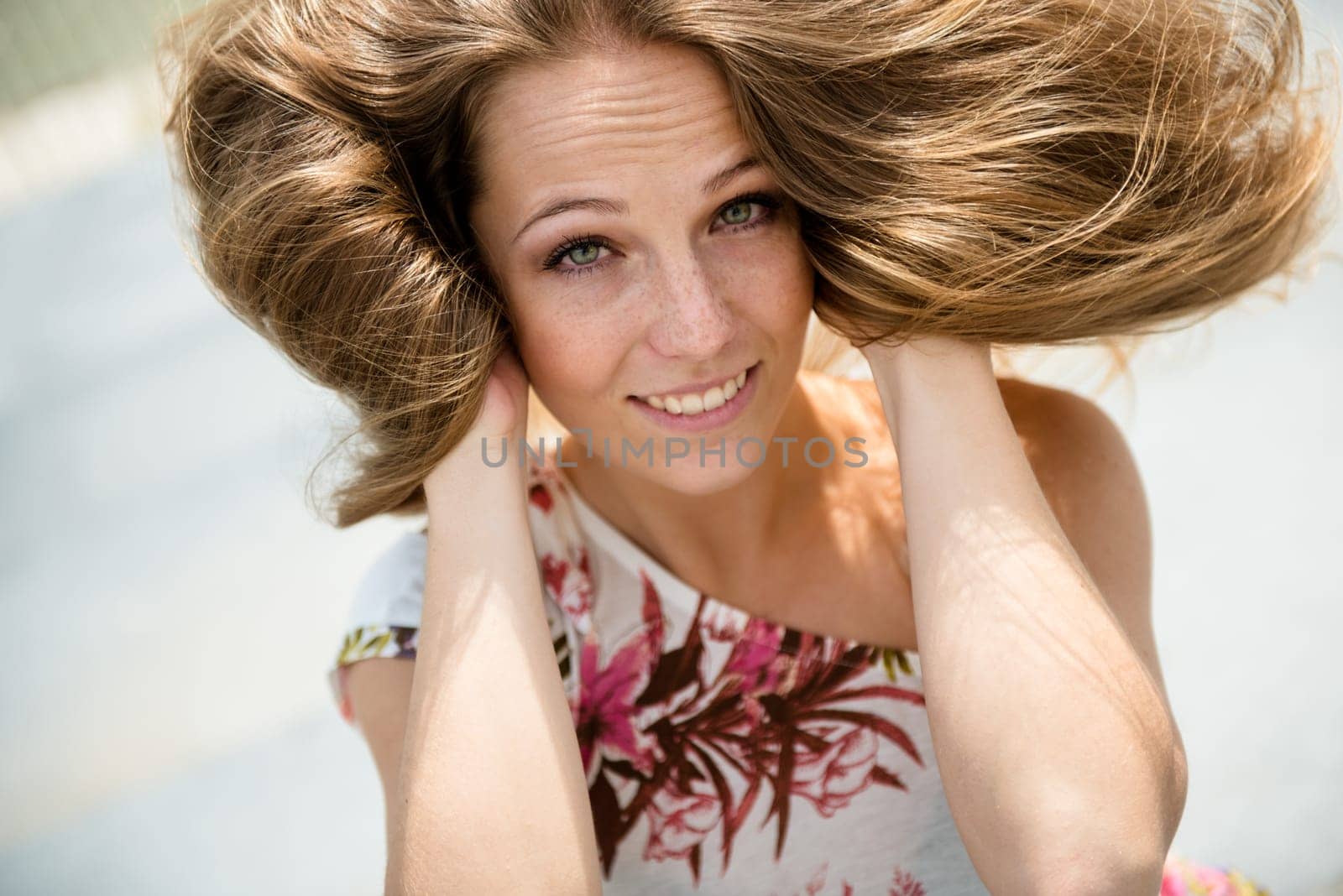 Outdoor portrait of young happy smiling woman playing with hair