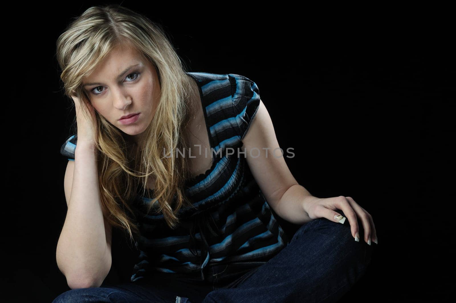 Young blond woman (teenager) in depression isolated on black background