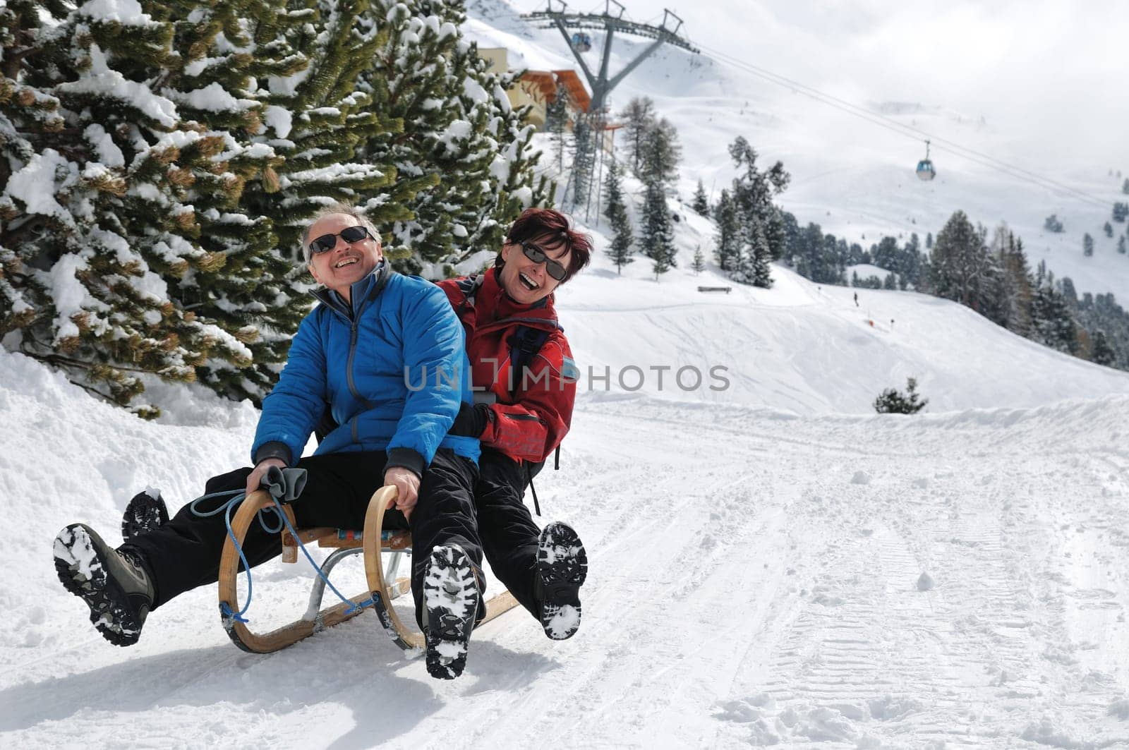 Active senior couple on sledge having fun in mountain snowy country